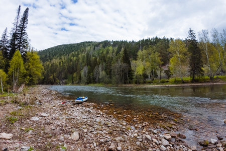 In this serene river scene, a small boat floats along the water, bordered by a rocky shoreline and vibrant trees. Its a picturesque view for nature lovers seeking peace and beautyの写真素材