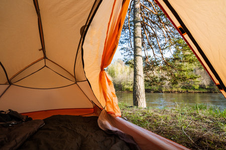Imagine a serene view from a cozy tent, with a peaceful river flowing through lush nature, perfect for camping trips and outdoor adventures like hiking, fishing, or relaxing by the riverbankの写真素材