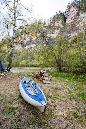 A tranquil lakeside scene features a blue kayak on the sandy shore, surrounded by lush greenery and cliffs, ideal for outdoor enthusiasts and nature lovers to unwind and enjoy a perfect dayの写真素材
