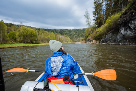 A person in a blue waterproof jacket is kayaking on a beautiful river, surrounded by lush greenery and steep cliffs, experiencing the tranquility of nature and the spirit of outdoor adventureの写真素材