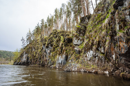 This breathtaking view features a stunning riverbank with rugged cliffs adorned in lush greenery and tall trees, creating a serene and picturesque landscape that captivates the imaginationの写真素材
