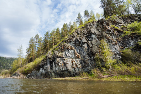 This serene river scene features a stunning rock formation surrounded by vibrant green trees, creating a picturesque landscape that captivates viewers and invites exploration of the environmentの写真素材