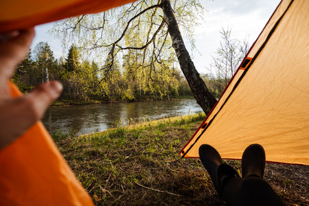Inside a cozy orange tent, one can enjoy a tranquil view of a picturesque riverside landscape with a...