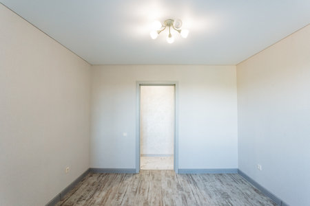 There is a completely empty room that features a door along with a bright light fixture situated on the ceiling, illuminating the space effectively. It creates a unique ambiance within the roomの写真素材