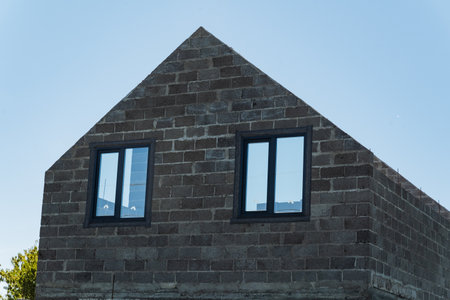 A sturdy and resilient brick building proudly stands with a distinctive triangular roof and two wellplaced, elegantly designed windows that enhance its charming and inviting architectural appealの写真素材