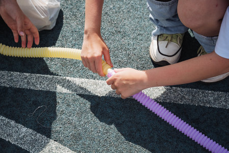 A person is joyfully playing with a long, bright yellow and purple inflatable tube, delighting in a sunny day spent outdoors, surrounded by a vibrant and cheerful atmosphere filled with laughterの写真素材