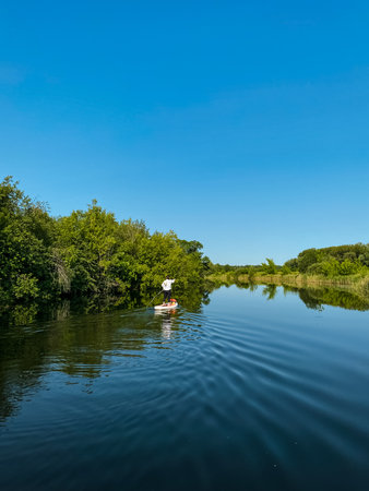 A person skillfully navigates a sturdy boat through a picturesque river, surrounded by vibrant trees...