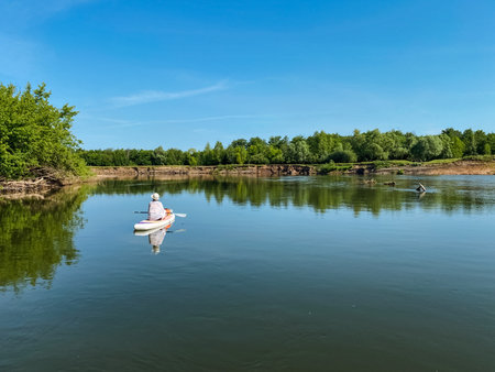 A person is currently rowing a kayak on a picturesque lake, enjoying the serene nature that surrounds them, including lush greenery and the calm, soothing waters flowing beneath their boatの写真素材