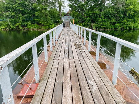 A beautifully crafted wooden bridge spans gracefully over a serene body of water, with lush trees thoughtfully positioned in the background, enhancing the picturesque viewの写真素材