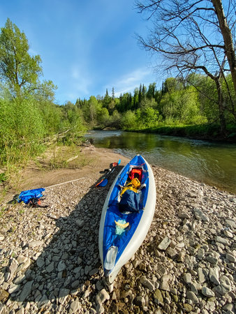 A vibrant blue and white kayak is currently resting on the rocky shore near a flowing river, creating a picturesque scene that captures the essence of outdoor adventure and recreationの写真素材