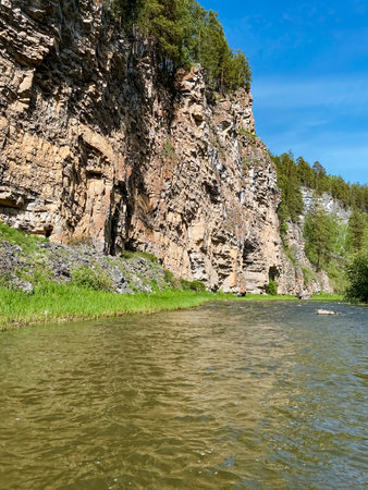 A beautiful and serene river is flowing gently through a stunning canyon, with a majestic cliff rising prominently in the background, creating a picturesque natural landscapeの写真素材