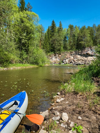 A colorful kayak is peacefully resting on the sandy shore of a beautiful river, waiting for its adventurous rider to take it for a thrilling ride on the water surfaceの写真素材