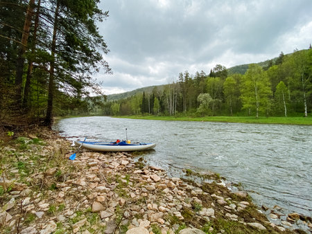A colorful kayak rests on a sandy river shore, surrounded by lush greenery and soothing nature sounds, creating a serene spot for outdoor enthusiasts to relax and enjoy the wildernessの写真素材