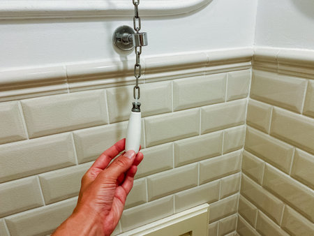 In a bathroom, an individual is holding a chain, possibly connected to a fixture or personal item, surrounded by various household hardware and tiled surfaces used for personal care activitiesの写真素材