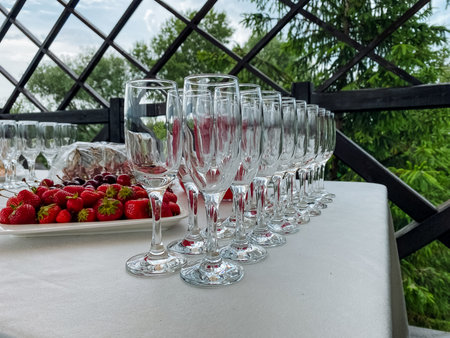 A beautiful collection of elegant wine glasses is arranged on a crafted wooden table, alongside fresh strawberries, ready for enjoyment during a special occasion, creating a delightful settingの写真素材