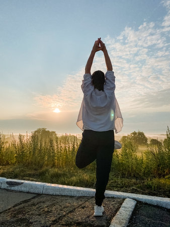 A woman is peacefully practicing her yoga routine on a stunning rooftop while the mesmerizing sunset casts its warm glow around her, fully embracing nature, tranquility, and inner blissの写真素材