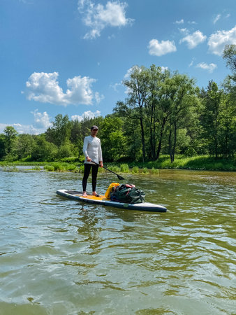 A man is currently standing on a paddle board in the water, skillfully maintaining his balance while enjoying a peaceful moment in nature, surrounded by the beauty of the open waterの写真素材