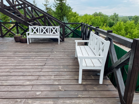 There are two white benches located on a spacious wooden deck, providing an inviting spot for relaxation and enjoyment of the surrounding area, perfect for social gatherings or quiet contemplationの写真素材