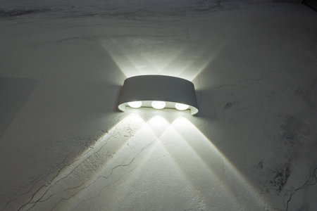 A bright and elegant white wall light fixture is illuminating a pristine white wall, creating a warm and inviting atmosphere that can enhance any interior space with its soft glowの写真素材