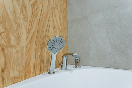 A shower head, which is an essential plumbing fixture, is securely attached to the side of a bathtub, providing a convenient way to enjoy bathing or rinsing off while in the bathroomの写真素材