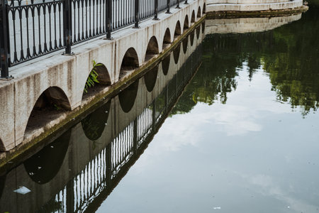 A picturesque bridge gracefully spans a tranquil body of water, where lush trees are beautifully reflected in the still surface of the water, creating a serene and scenic landscapeの写真素材
