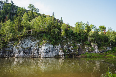 Imagine a serene lake that is beautifully surrounded by trees and rugged rocks, nestled right in the heart of a lush forest, creating a peaceful natural oasis that invites tranquility and reflectionの写真素材