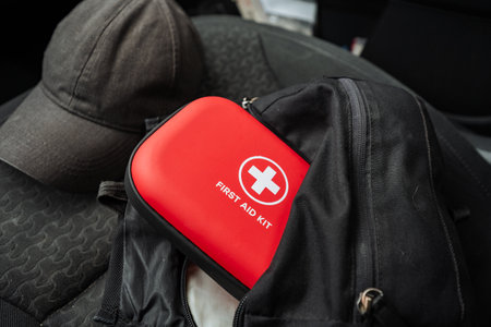 A bright red first aid kit is placed neatly on top of a durable black travel backpack, which serves as a vital item for providing immediate medical assistance whenever it is needed mostの写真素材