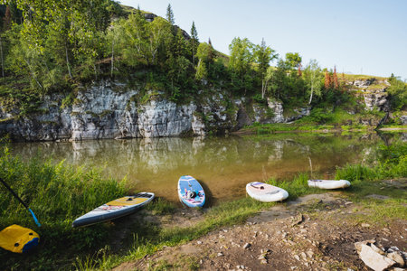 Three paddle boards are currently resting on the sandy shore of a beautiful lake, waiting for someone to take them out for a fun day on the water and enjoy the picturesque scenery around themの写真素材
