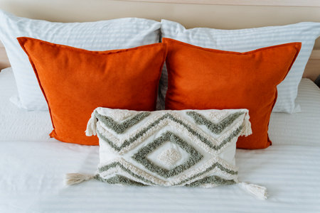There is a comfortable bed adorned with vibrant orange pillows alongside a pristine white pillow situated comfortably on it, creating a cozy and inviting atmosphere in the bedroomの写真素材