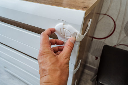 A person is currently holding onto a child safety lock that is firmly attached to a dresser, making...