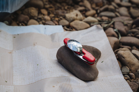 A vibrant red knife rests on a smooth stone, showcasing its sleek multifunctional design for outdoor...