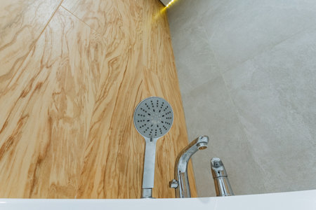 A beautifully designed shower head can be seen resting elegantly on a polished wooden counter that is conveniently situated next to a luxurious bathtub, creating a serene bathing environmentの写真素材