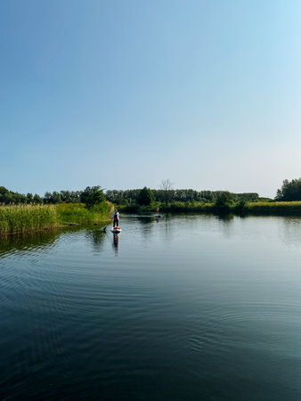 A person is happily riding a paddle board on a serene lake, enjoying the beautiful scenery that...
