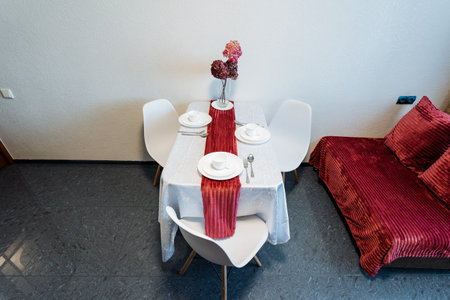 In a cozy living room setting, there is a stylish table accompanied by a set of chairs, all complementing the vibrant red couch that adds a pop of color to the space, creating a warm atmosphereの写真素材