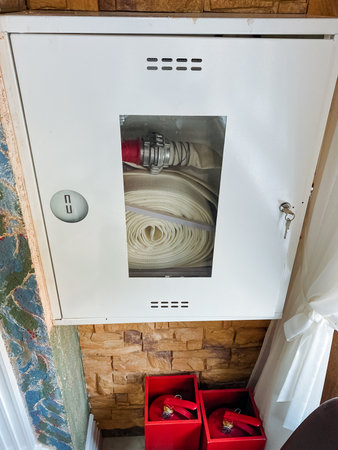A sturdy fire hose is currently resting inside a clean, white cabinet, which adds a touch of organization to the area. This cabinet serves as a home for various safety equipment and suppliesの写真素材