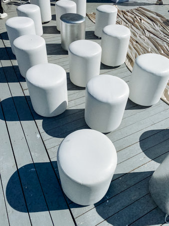 A meticulously arranged collection of white ottomans is placed upon a beautifully crafted wooden deck, creating an appealing and stylish outdoor space that invites relaxation and enjoyment for allの写真素材