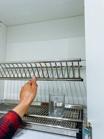 A person is carefully placing a glass of refreshing water onto a dish rack that is designed for drying dishes effectively and efficiently, making use of available space in the kitchenの写真素材