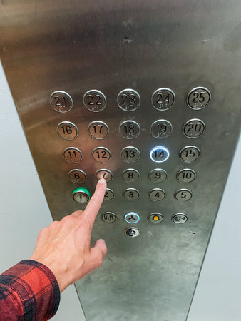 In a moving elevator, a person can be seen continuously pressing a bright green button, which is a typical feature found in numerous residential and commercial buildings around the areaの写真素材