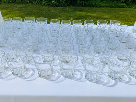 A beautiful arrangement of elegant glass cups on a white tablecloth in a vibrant green garden creates the ideal scene for cherished gatherings and special events to remember for yearsの写真素材