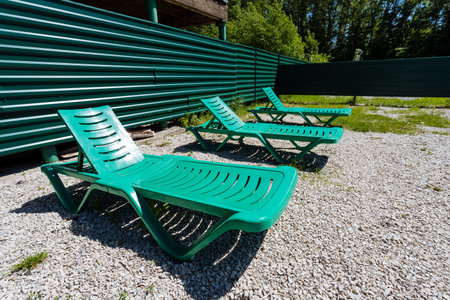 Three green lounge chairs are aligned along a gravel path, surrounded by lush greenery, creating a warm, inviting spot for relaxation in a serene outdoor environment during the dayの写真素材