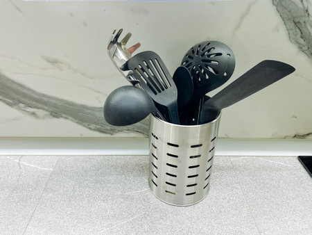 A gleaming stainless steel utensil holder is filled to the brim with a variety of black kitchen utensils, providing both a stylish and practical solution for organizing kitchen tools and gadgetsの写真素材