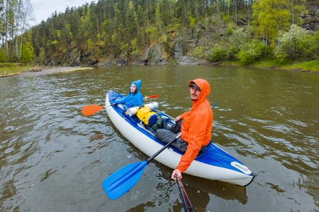 Two adventurers immerse themselves in a thrilling kayaking trip along a peaceful river, embraced by vibrant greenery and stunning rocky landscapes, creating the perfect outdoor getaway experienceの写真素材