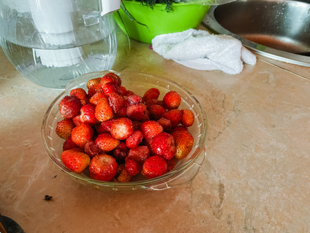 A bright and colorful bowl filled with ripe strawberries is placed on a counter, right next to a pitcher of sparkling water, making for a refreshing and appetizing display of fresh produceの写真素材