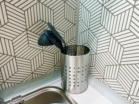 The beautifully designed kitchen features a sleek stainless steel sink with a durable utensil holder atop the counter, adding a contemporary touch and enhancing the kitchens modern aestheticsの写真素材