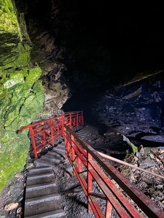 There are stairs that lead up to a mysterious and intriguing cave, featuring a striking red railing that adds a touch of color to the natural surroundings and enhances the overall aesthetic appealの写真素材