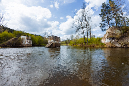 This striking view features decaying structures by a serene river, surrounded by vibrant greenery and a captivating sky, ideal for exploring environmental and architectural themesの写真素材