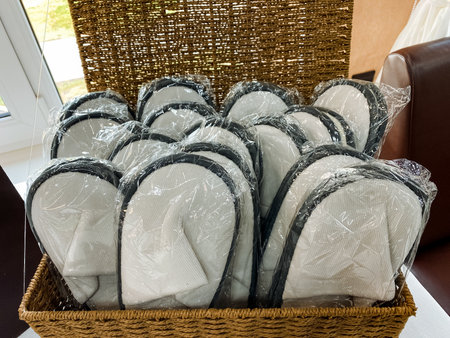 A beautifully crafted basket that is filled with a collection of white slippers, all carefully wrapped in protective plastic, ready for storage and to keep them clean and organizedの写真素材