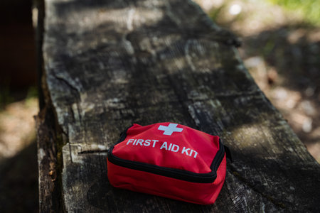 On a sturdy wooden bench, there is a bright red first aid kit placed prominently for easy access in...