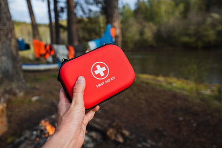 A vibrant red first aid kit held outdoors, showing preparedness for camping, hiking, and other adventures by the river. Essential for safety in natureの写真素材