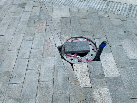 A cracked pavement has exposed an open manhole cover, posing a serious risk to pedestrians. Cautionary measures are essential to prevent accidents and injuries, ensuring public safety for allの写真素材